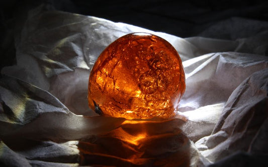 Pierre d'ambre roulée, présenté sur un tissu papier froissé avec la lumière qui traverse la pierre par derrière , qui permet de voire ses nervures.