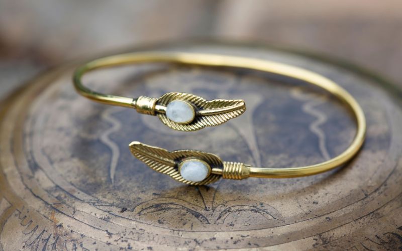 Bracelet style jonc couleur doré en acier inoxydable, avec deux pierres naturelles semi-précieuse blanche, posé sur un objet en cuivre.