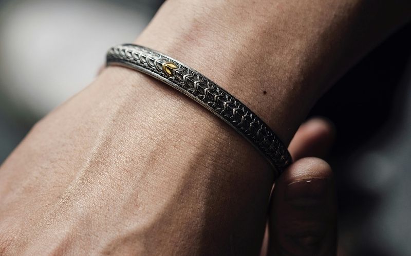 Zoom sur le poignet d'un homme, qui porte un bracelet rigide en métal.