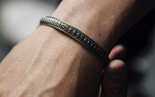 Zoom sur le poignet d'un homme, qui porte un bracelet rigide en métal.