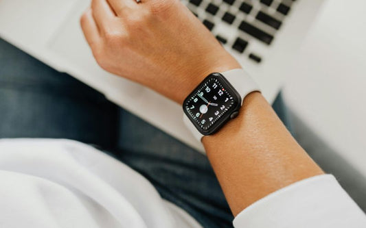 bras d'homme portant un braceletet une apple watch homme qui affiche l'horloge aiguille, on voit son ordinateur en arrière plan flou.