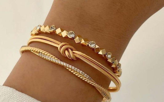 Poignet d'une femme qui porte trois bracelets, dont deux en chaine. Ils sont tous dorés et fins.