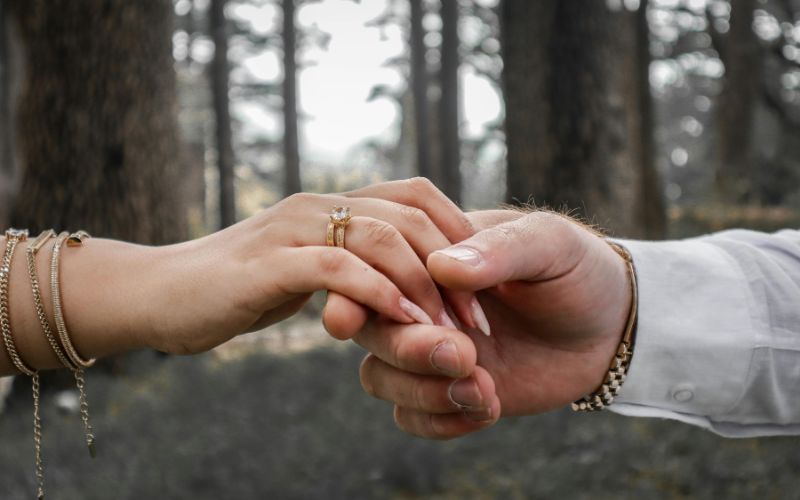 main d'une femme tennue par la main d'un homme avec la forêt en arrière plan. chacun porte plusieurs bracelets  dont un bracelet couple