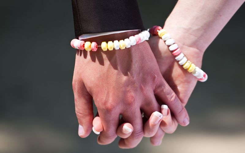 Photo de deux mains qui se tiennent, chacun porte un bracelet en perles bonbon.