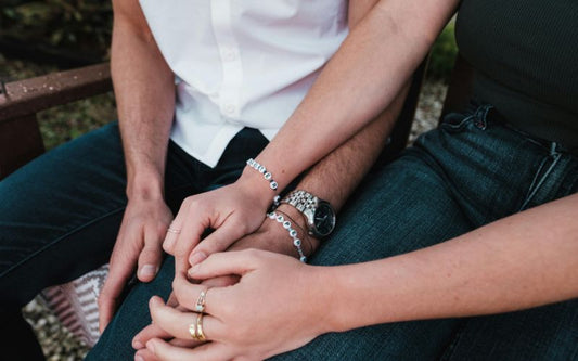 Couple homme et femme assis se tenant la main avec un bracelet couple avec des perles lettres gravées