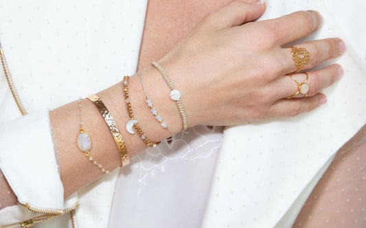Bras femme avec cinq bracelets doré et blanc, sur un haut blanc.