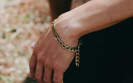 Poignet et avant bras d'homme qui porte un gourmette en argent doré à grosse maille et plaque non gravée.