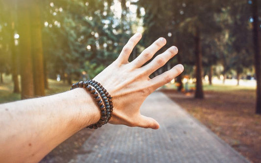 Homme qui tend le bras la main ouverte devant lui, on arrière plan on voit une forêt, il porte trois bracelets en perles pour homme.