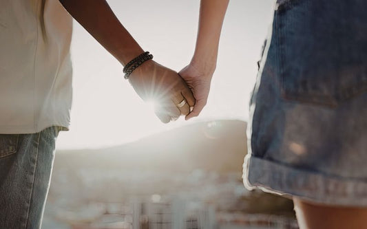 Un homme et une femme qui se tiennent la main. on ne voit que leur mains et leur avant bras. l'homme porte un bracelet en perle homme noir avec un autre bracelet marron.
