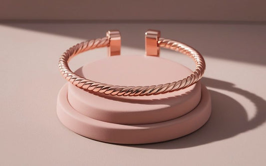Superbe bracelet jonc rosé doré torsadé, posé sur un présentoir rond rose pastel avec la lumière du soleil qui l'éclaire.