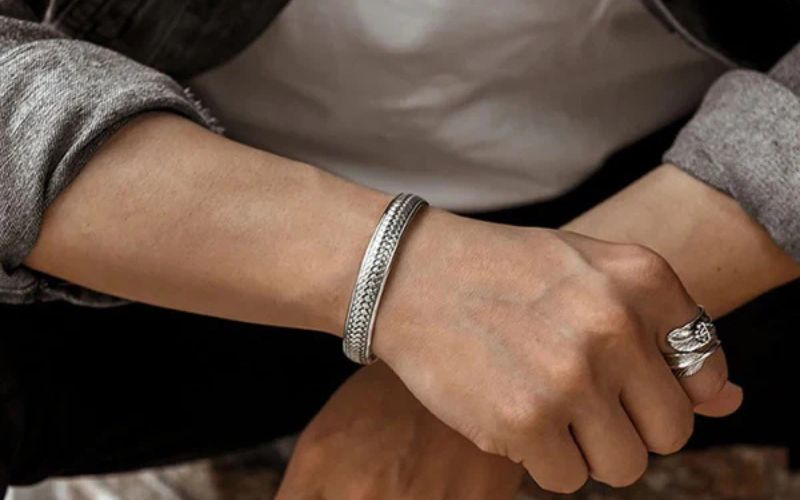 Homme portant un bracelet jonc homme argenté et une bague. on ne voit que son avant bras et son poignet : https://maison-bracelet.com/products/bracelet-jonc-homme-argente-gravures-internes