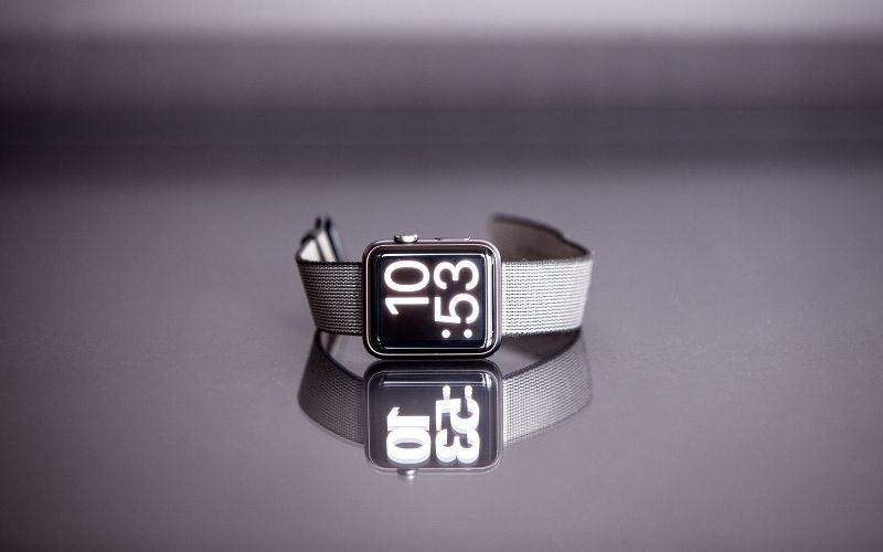 Montre Samsung Galaxy Watch avec bracelet en acier inoxydable, présenté sur une table grise effet miroir sur lauqelle on voit le reflet de la montre et du bracelet.