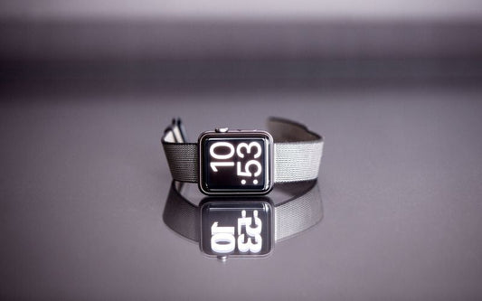 Montre Samsung Galaxy Watch avec bracelet en acier inoxydable, présenté sur une table grise effet miroir sur lauqelle on voit le reflet de la montre et du bracelet.