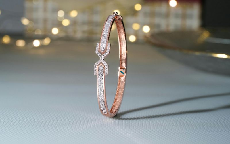 Bracelet rigide tenant tous seul debout, mélange de cuivre et de strass zircon et une personnalisation au niveau di fermoir à l'intérieur. on voit guirlande lumineuse en arrière plan flou.