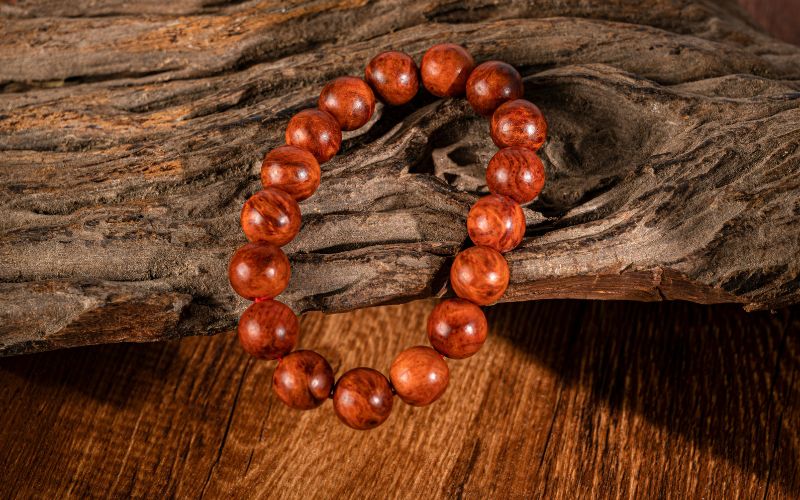 Bracelet en bois marron, perles rondes assez grosses, posé sur une souche de vigne et une table en bois