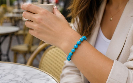 Avant bras femme, portant une tasse de café et un bracelet en perle ronde de pierre turquoise, elle est assise à un café en terrasse