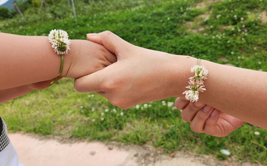 Photo de deux mains qui se tiennent fille et mère, qui se sont fait des bracelets fleurs pour offrir chacune à l'autre.
