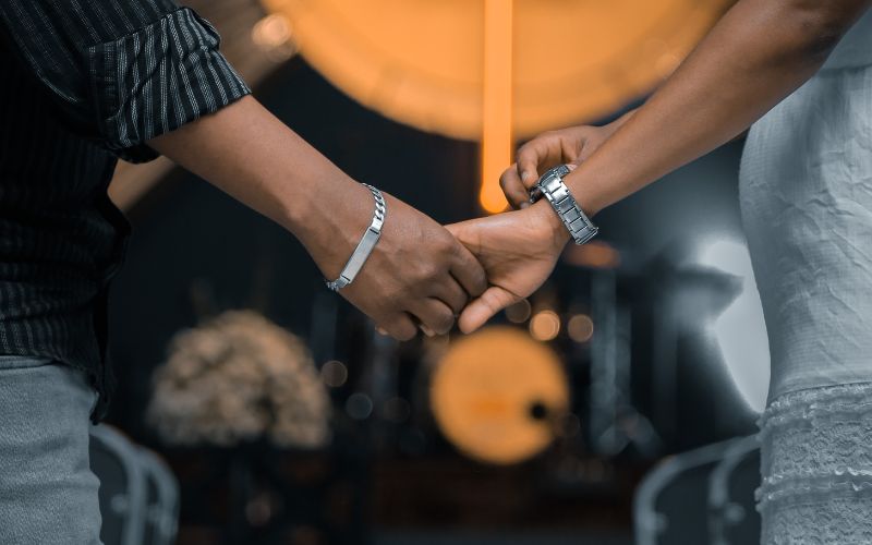 deux personne qui se tiennent la main, un homme qui porte une gourmette en argent et une femme qui porte une montre en argent. on ne voit que leur bras et leurs mains.