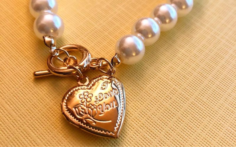 Bracelet saint valentin avec cœur gravée dorée, message d'amour et perle blanche. sur papier beige.