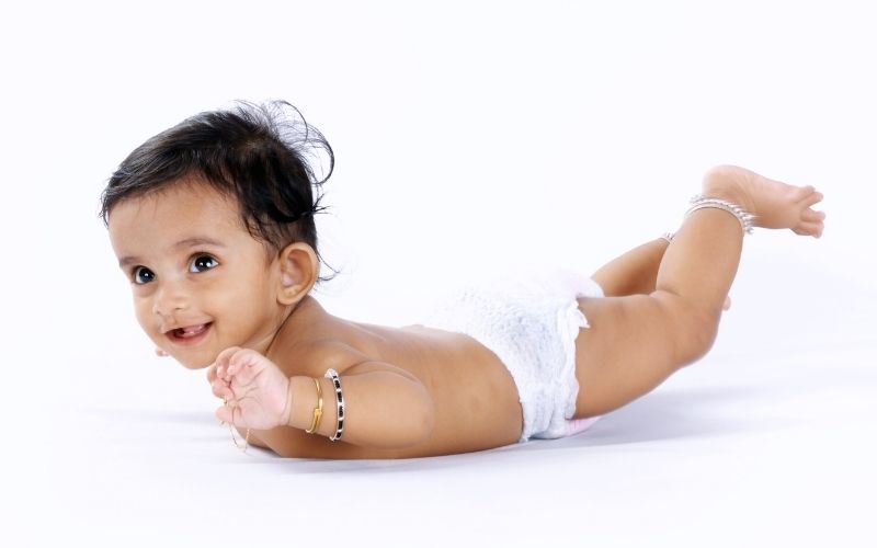 bébé allongé sur le ventre portant une couche et deux jolis bracelets, il sourit, sur un fond blanc