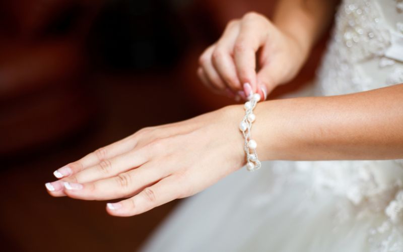 Bras de femme, avec bracelet délicat avec perle blanche et effet feuille. Le fond est flou.