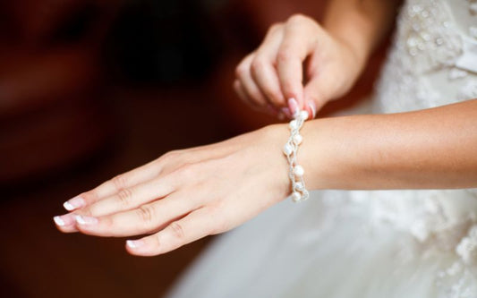 Bras de femme, avec bracelet délicat avec perle blanche et effet feuille. Le fond est flou.