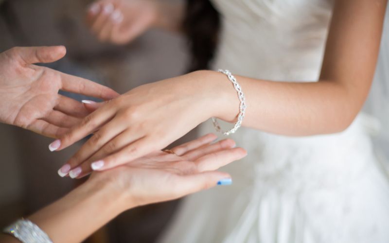 Poignet d'une femme en robe de mariée, qui porte un bracelet très élégant, les mains de l'autre femme entoure le bracelet.